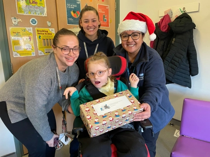 3 Staff Members Sharing A Present With A Child