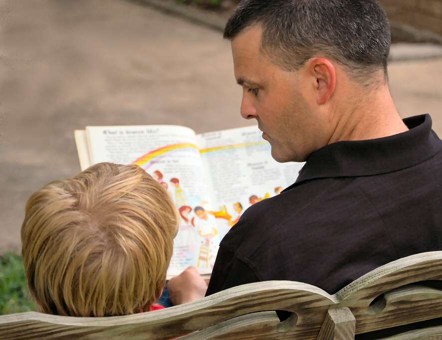Dad reads a book to his son - photo taken from behind as if someone looking on