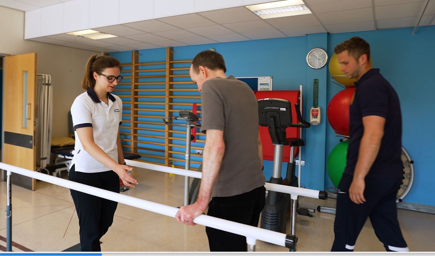 Physio and student supporting patient on walking frame