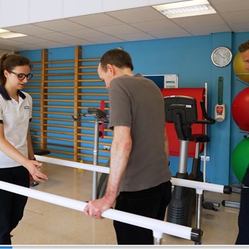 Physio and student supporting patient on walking frame