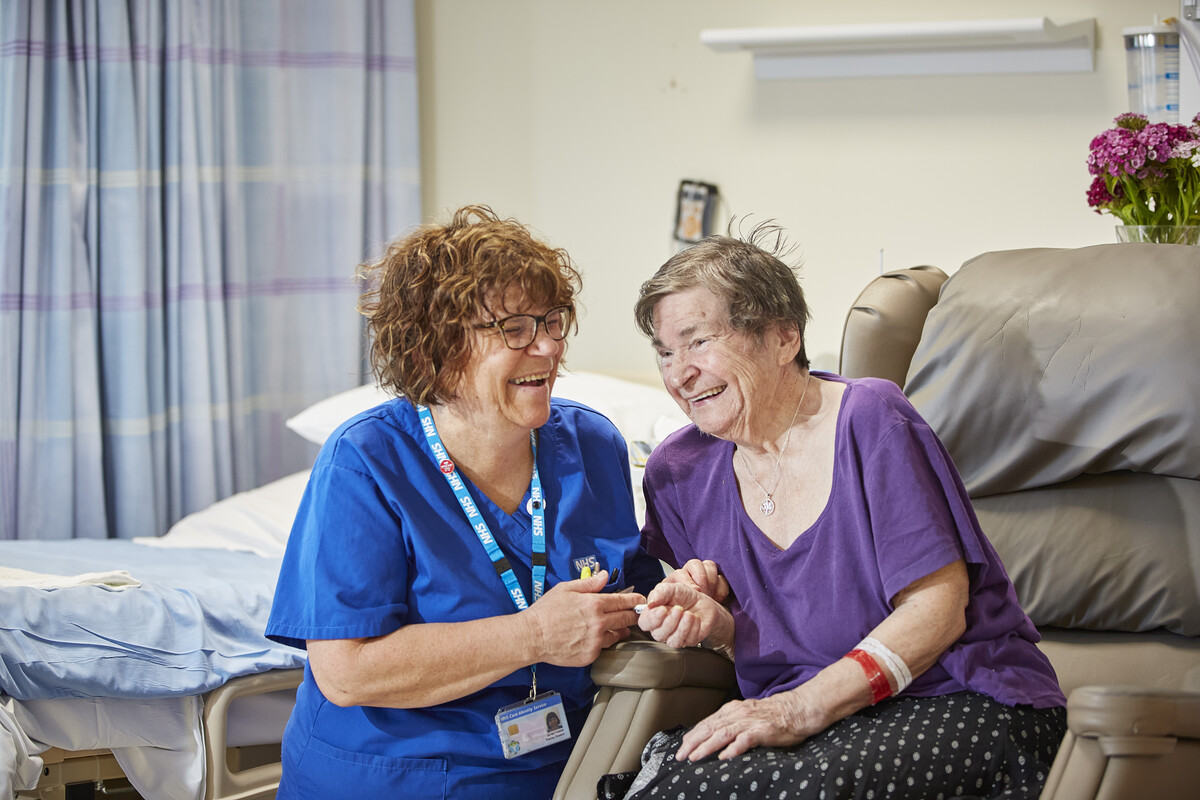 A photo of a nurse, smiling and comforting an older patient, in an inpatient ward
