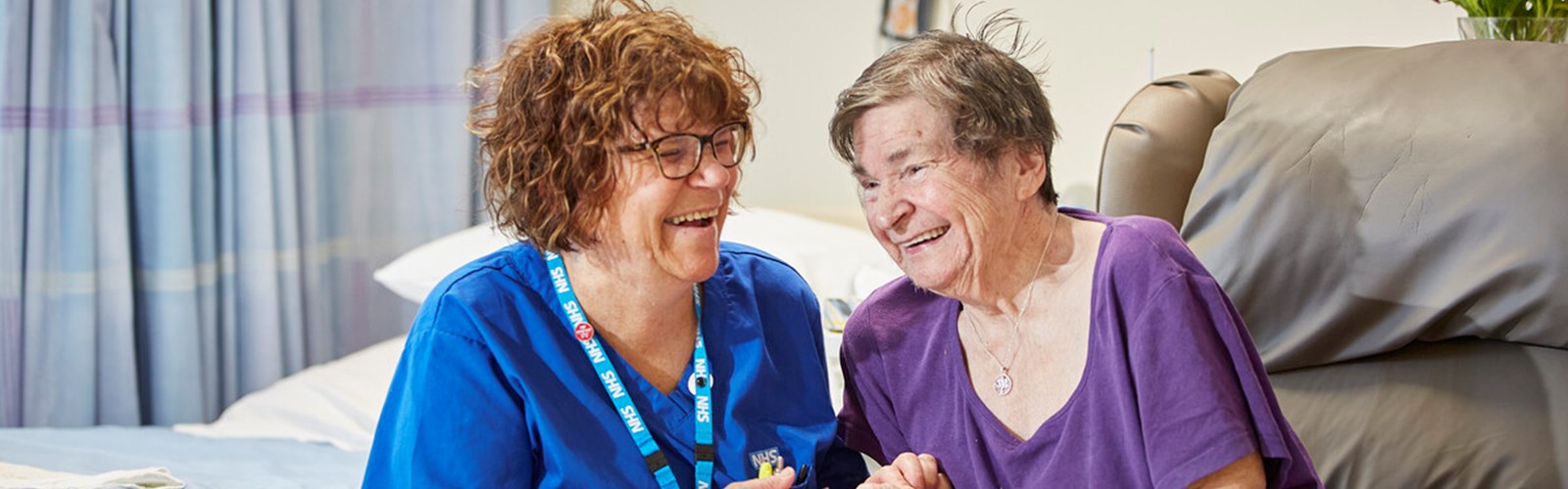 A photo of a nurse, smiling and comforting an older patient, in an inpatient ward
