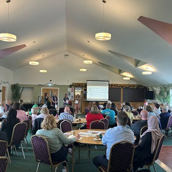 Event space with lots of attendees. One person presenting to the group.