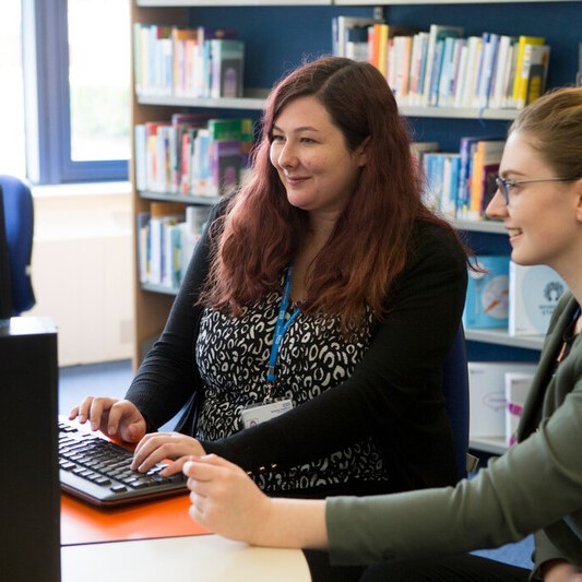 Two women sat at a desk, smiling, looking a computer monitor