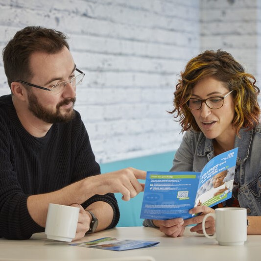 Two people sat, drinking a cup of tea, while reading a leaflet about onboarding