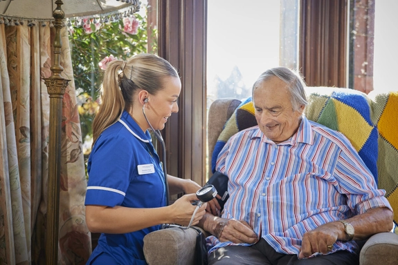 Nurse with stethoscope checking Blood Pressure in Elderly Patient's Home