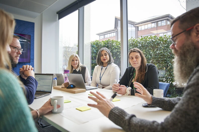 Staff around a table in a meeting with laptops