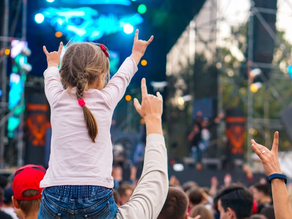 Young girl at a loud live music event, on the shoulders of an adult and within a crowd